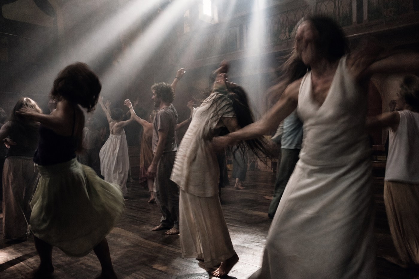 Barefoot dancers blurred with motion in a dark room, arms lifted toward nothing visible.