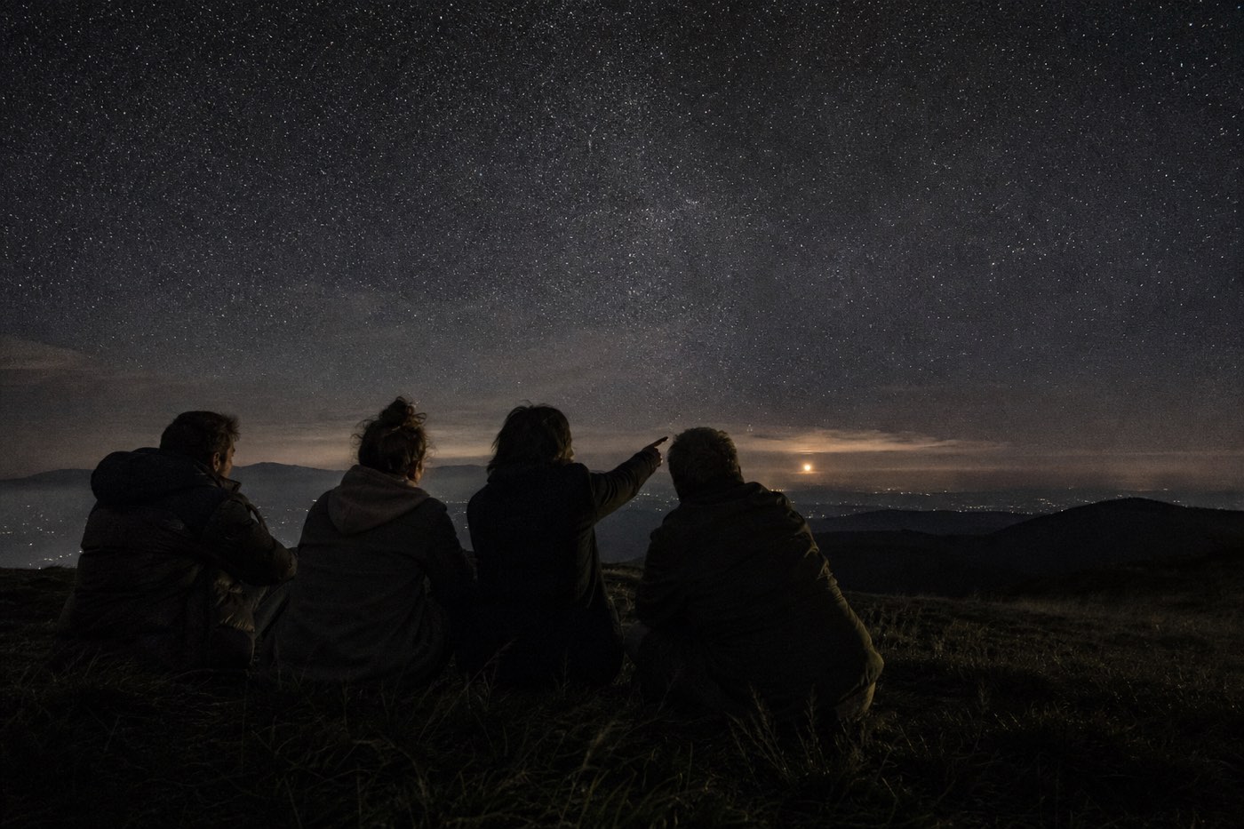 Figures on a dark hillside watching the night sky, waiting for ships.